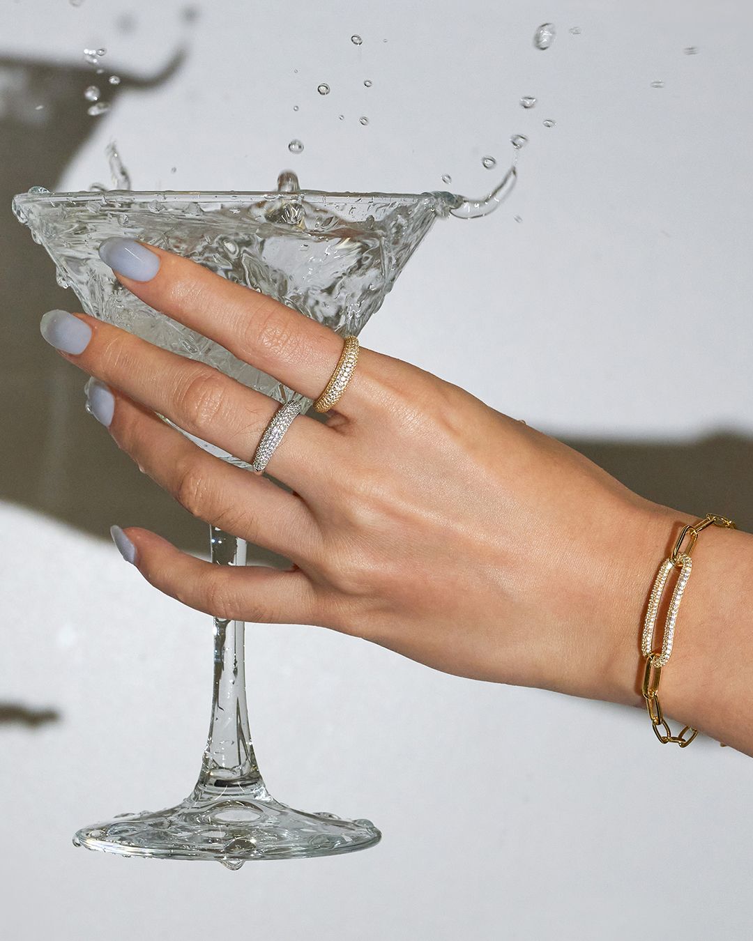 Main tenant un verre à martini, bijoux exposés, éclaboussures d'eau.