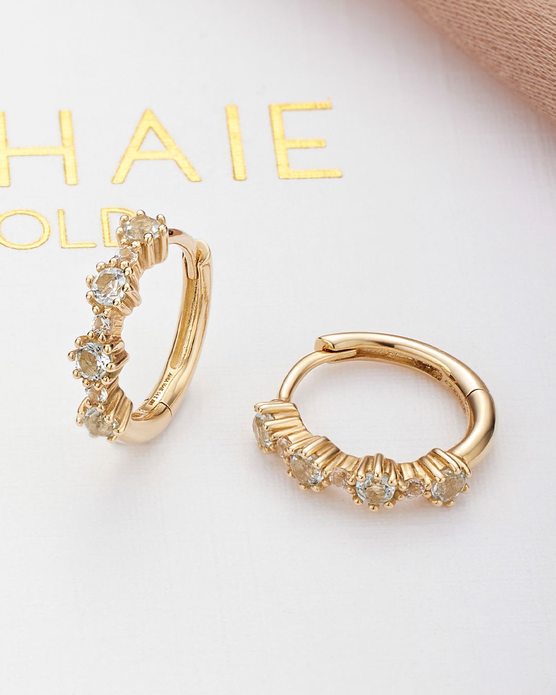 Boucles d'oreilles créoles en or avec petites pierres précieuses, sur une surface blanche.