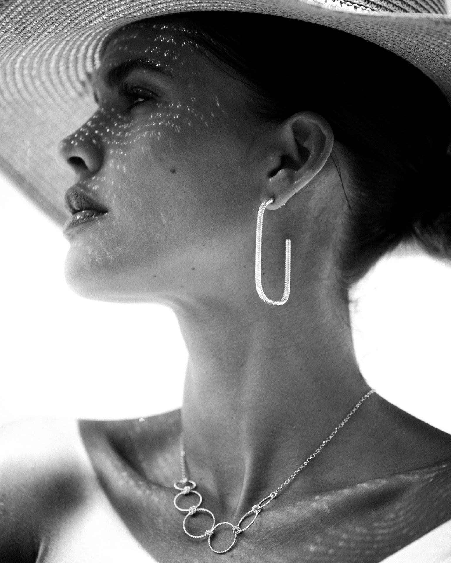 Femme portant un chapeau et des bijoux, levant les yeux, le visage ombragé.