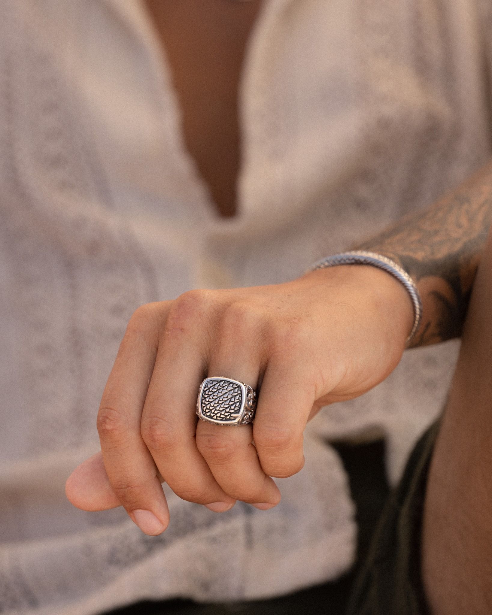Main d'homme avec une bague et un bracelet en argent ornés ; portant une chemise de couleur claire.