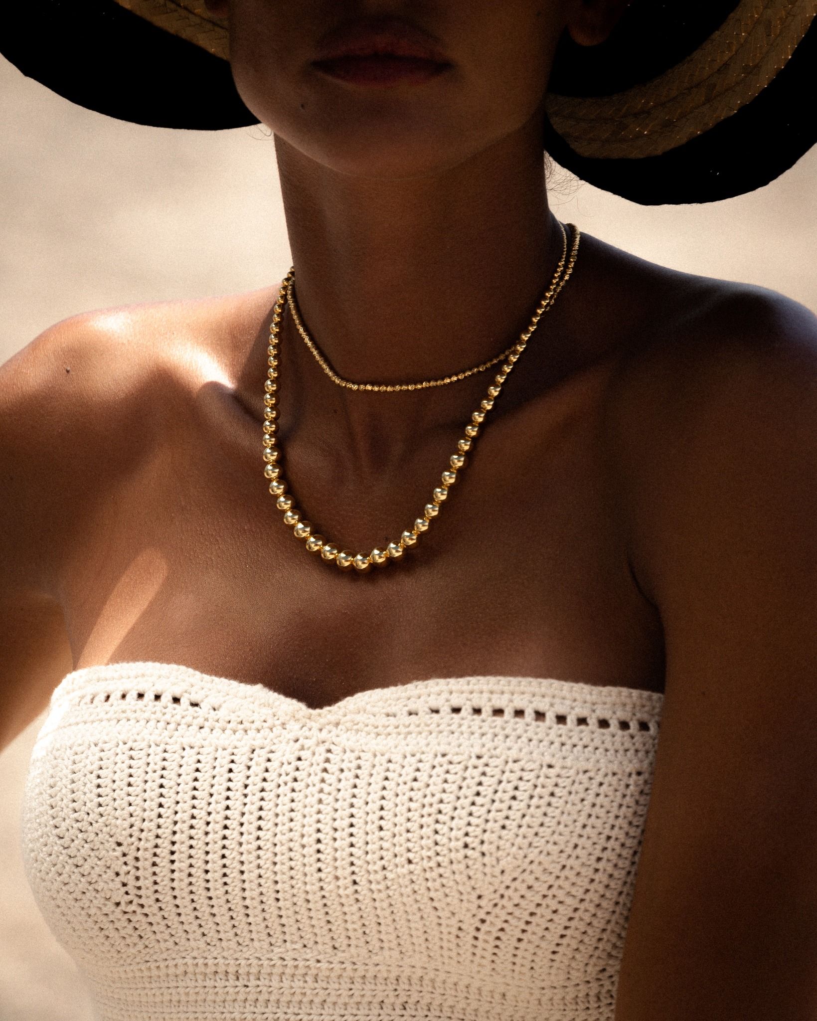 Femme en haut blanc au crochet et collier, portant un chapeau, à l'extérieur.