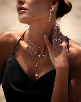 Femme portant des bijoux en argent : boucles d'oreilles, colliers et bagues. Elle porte une robe noire.