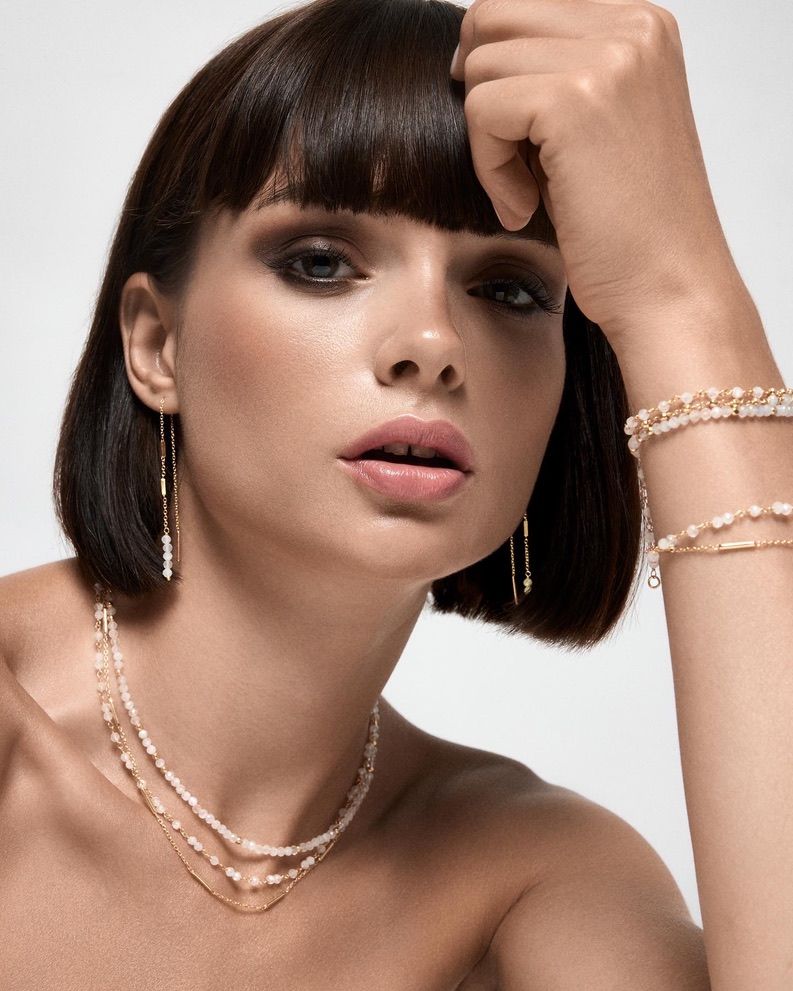 Femme avec un carré et un maquillage pour les yeux charbonneux, portant des bijoux en perles, regardant la caméra.