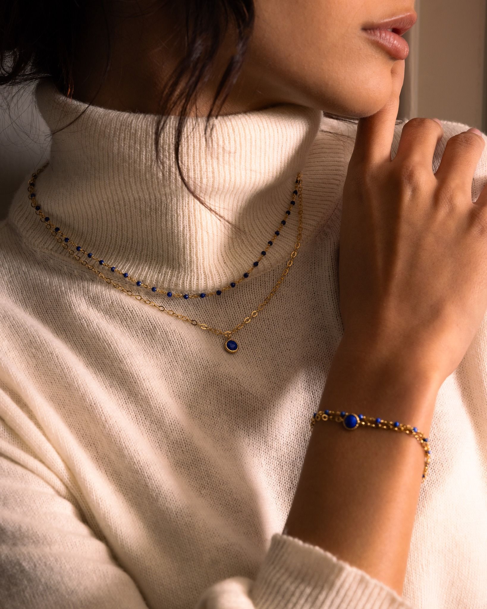 Femme portant des bijoux en or avec des pierres bleues; pull.
