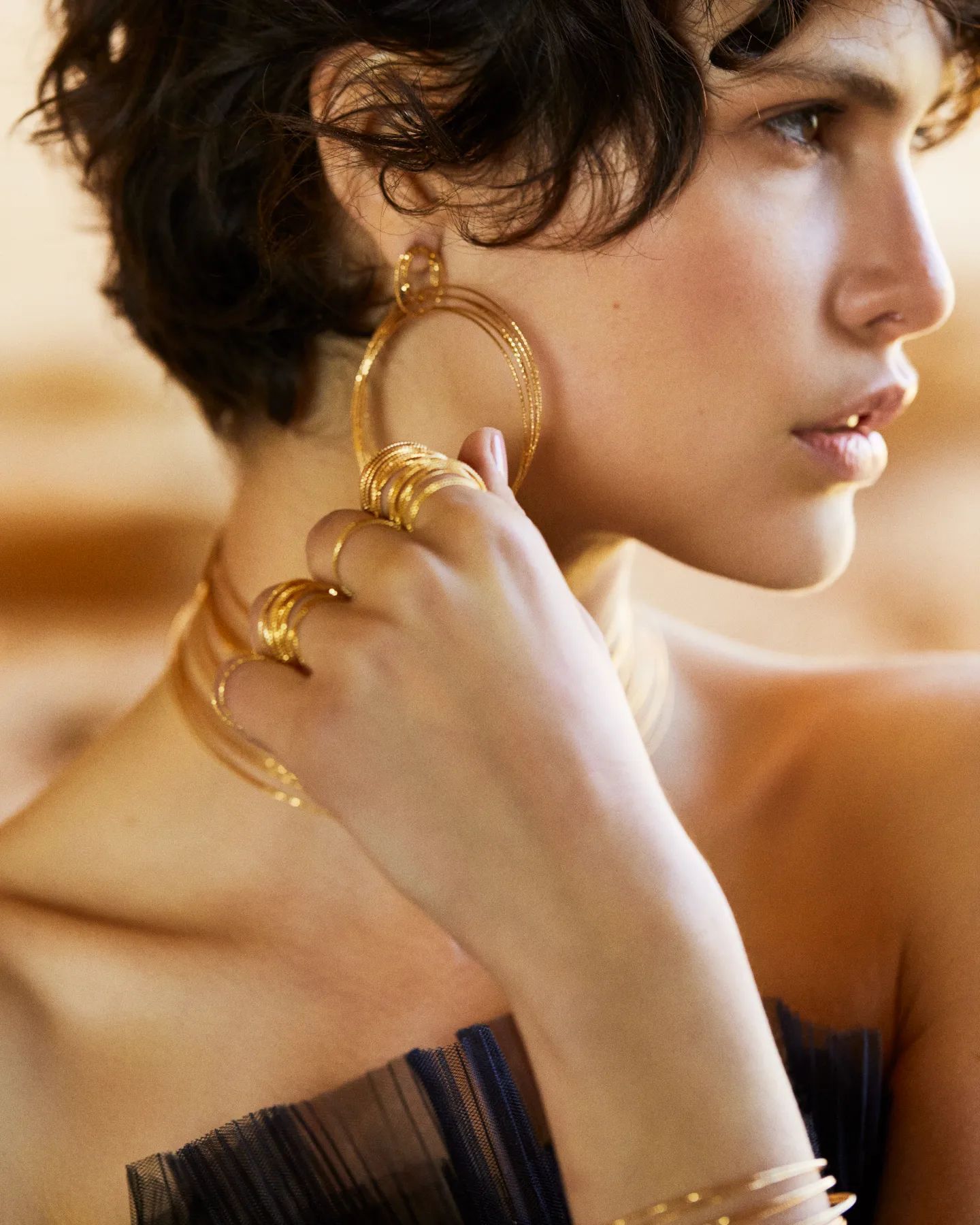 Femme aux cheveux noirs courts, portant des boucles d'oreilles créoles et des bagues en or, touchant la boucle d'oreille.