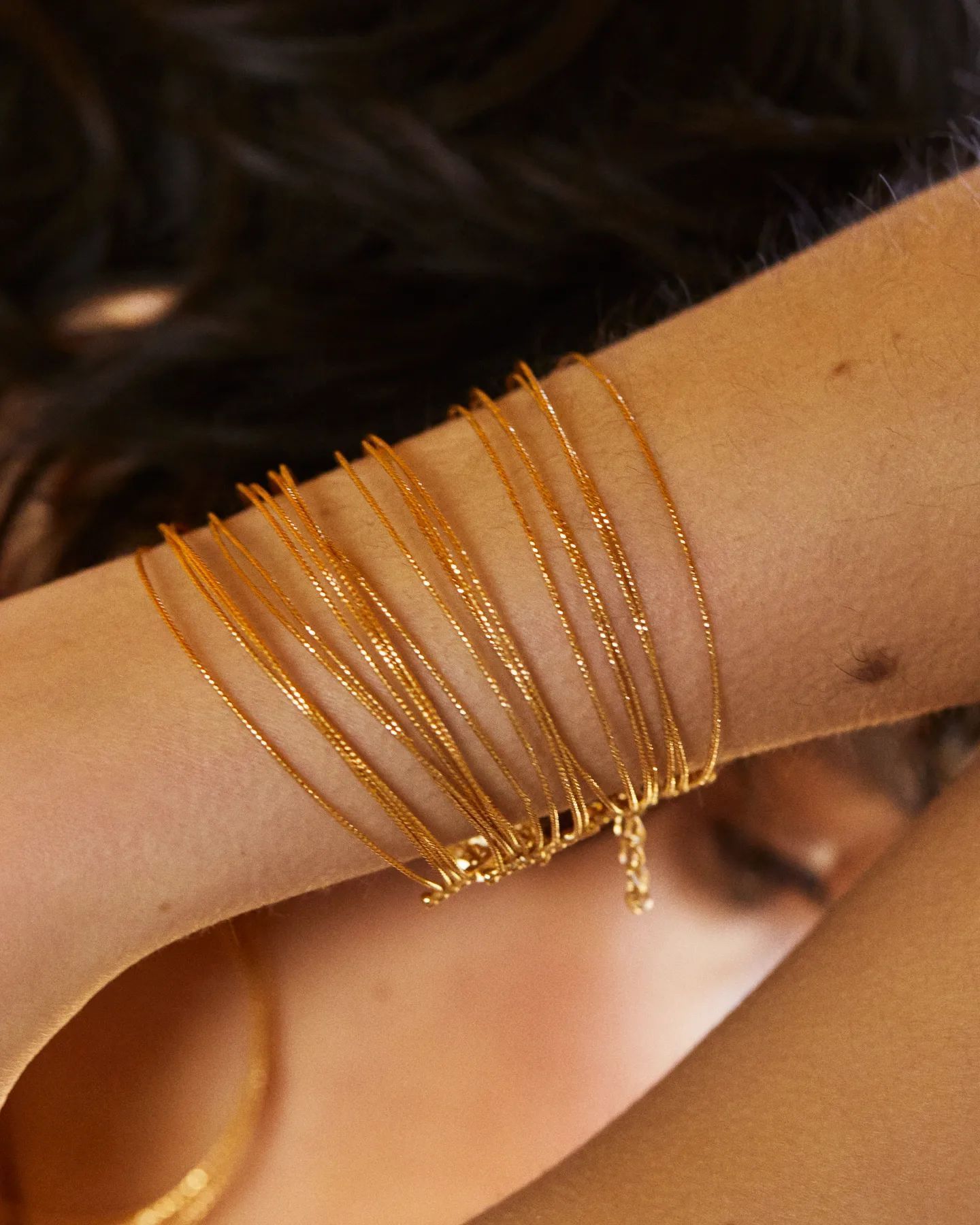 Bracelets en fil d'or sur le bras d'une personne, masquant partiellement le visage.