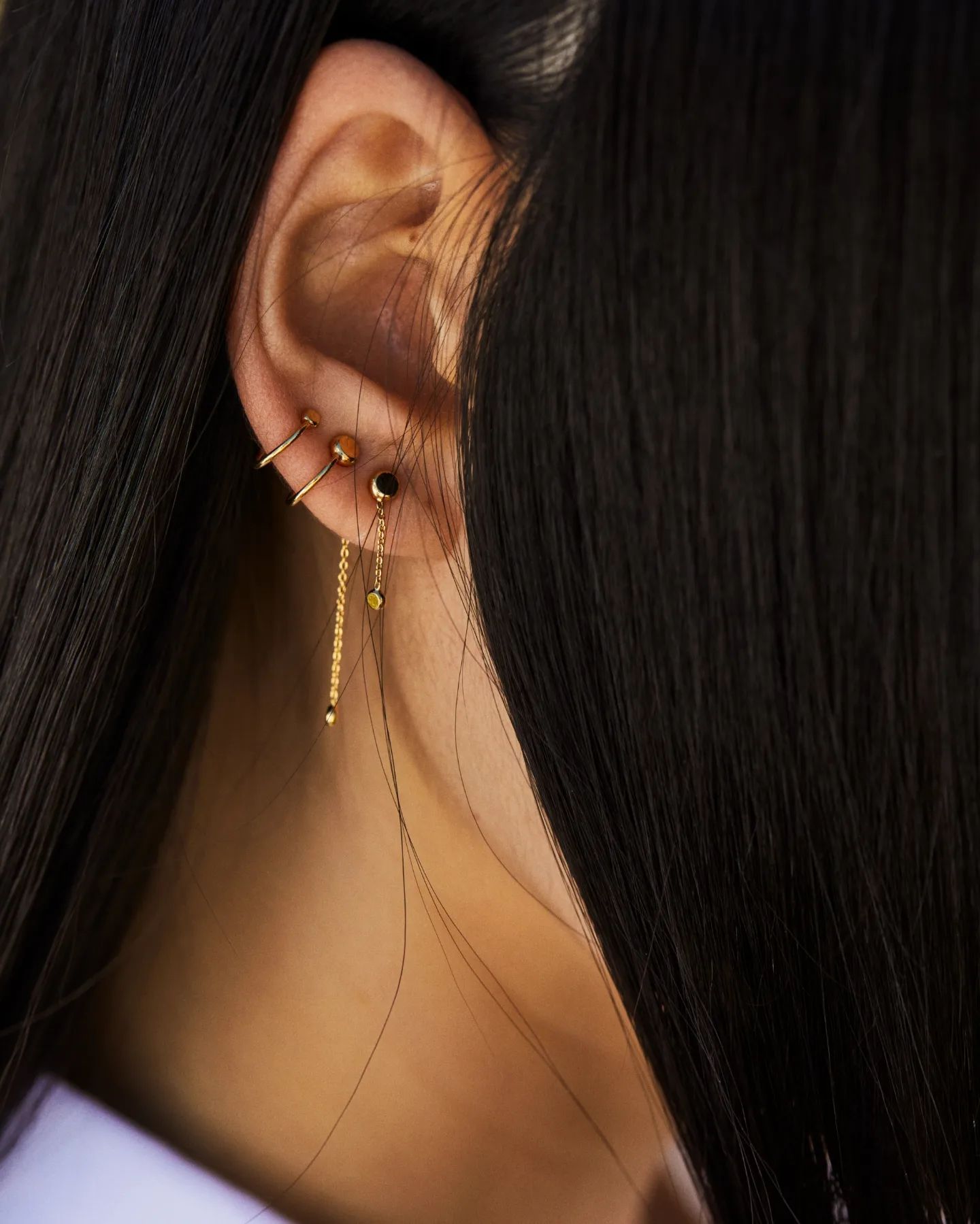 Oreille avec plusieurs boucles d'oreilles en or et cheveux foncés.