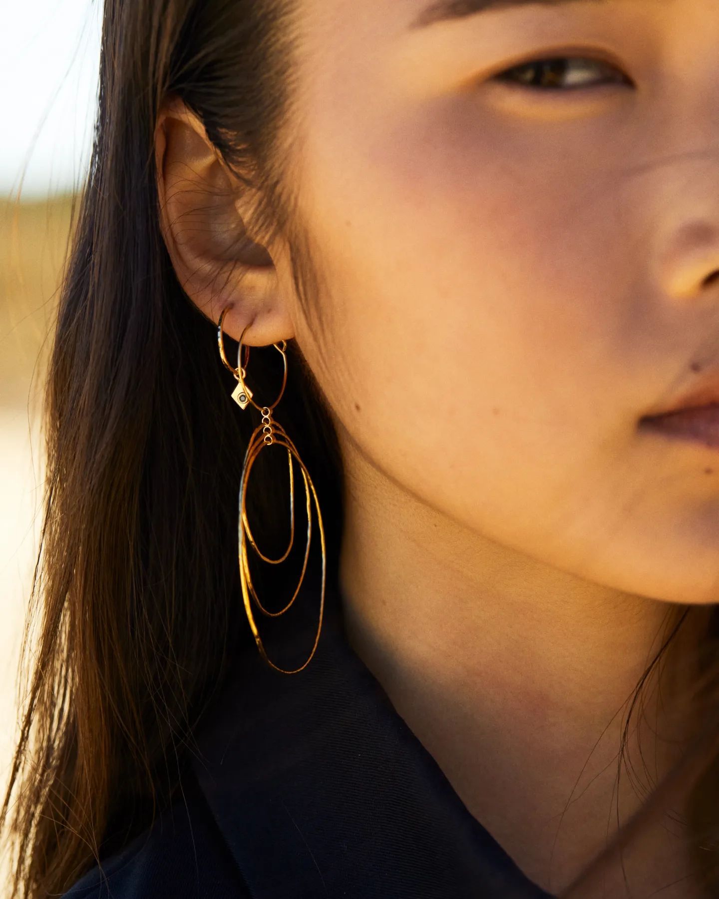 Femme avec des boucles d'oreilles en or, comprenant un ovale pendant et des créoles rondes plus petites.