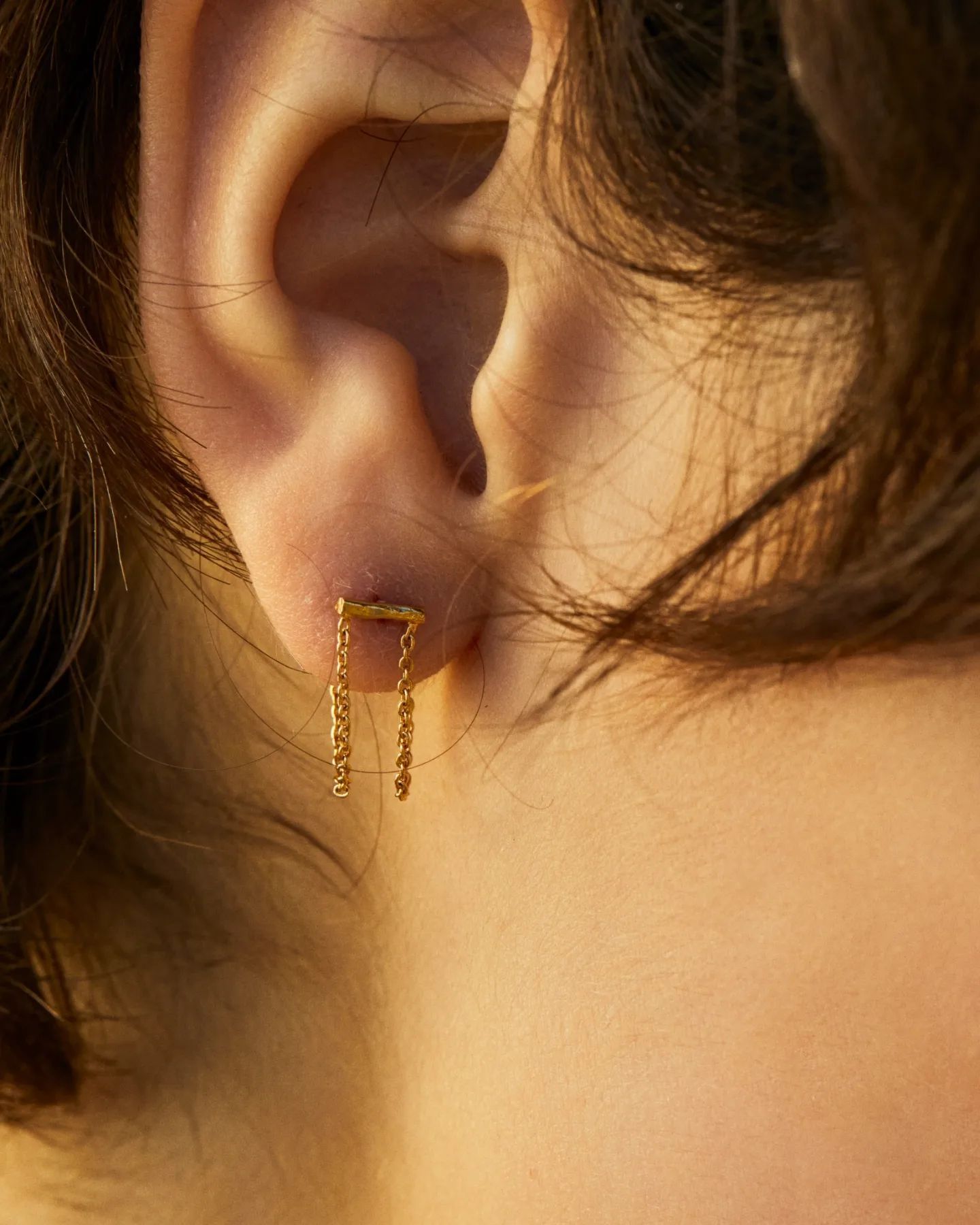 Gros plan d'une oreille avec une boucle d'oreille en or ; une barre horizontale avec une chaîne pendante.