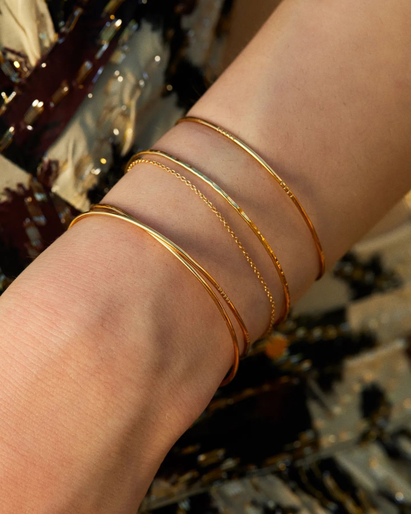 Bracelets en or sur un poignet, avec différentes textures, sur un fond à motifs.