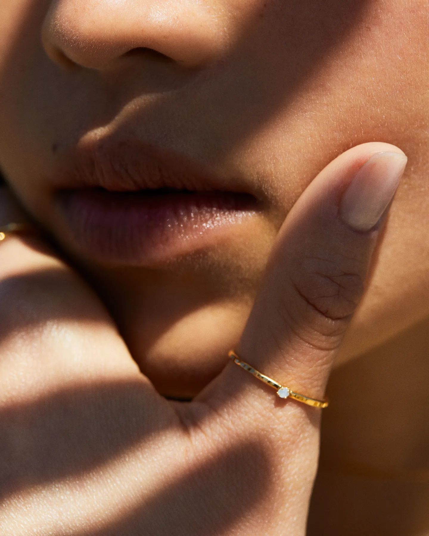 Gros plan des lèvres et de la main d'une personne avec une bague en or avec une petite pierre précieuse sur un doigt.