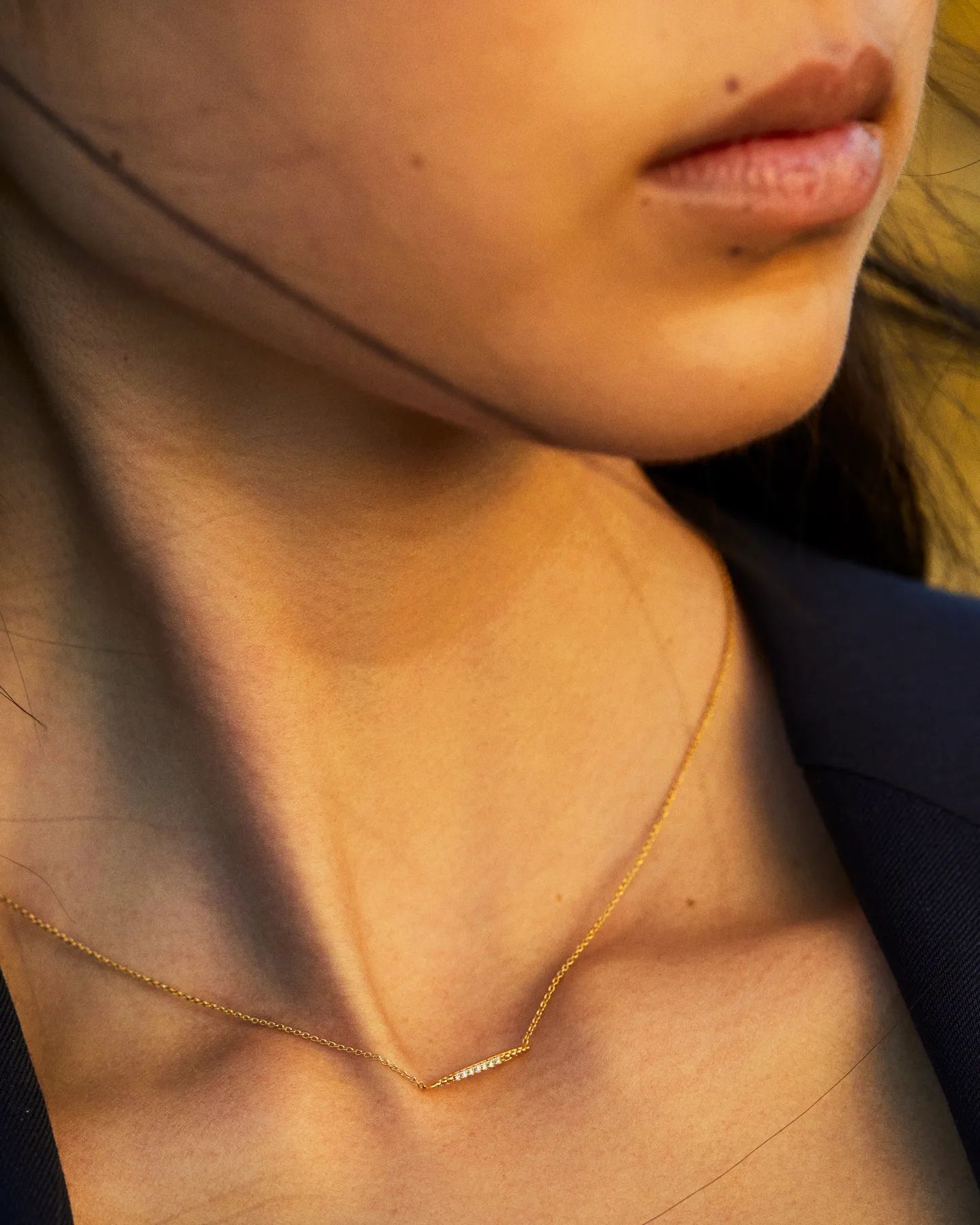 Gros plan du visage et du cou d'une femme, portant un délicat collier en or.