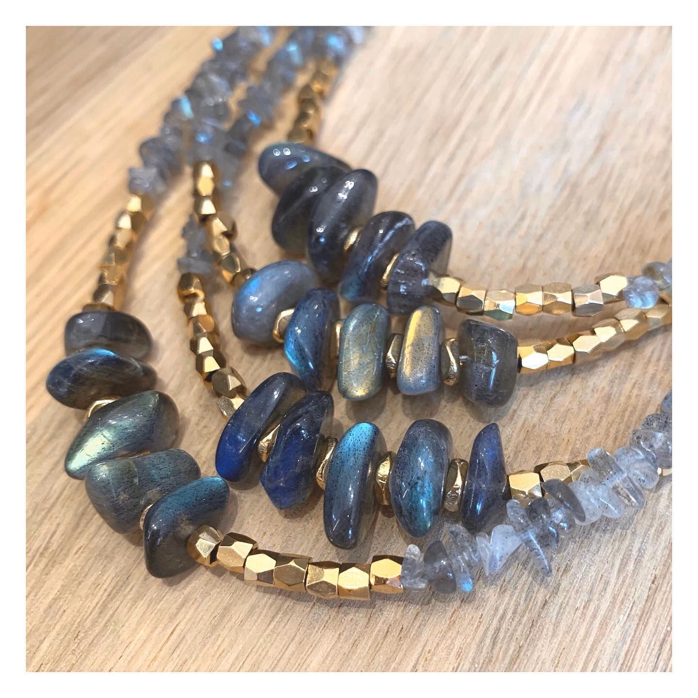 Collier à trois rangs avec perles d'or et pierres de labradorite bleue irisée sur une surface en bois.