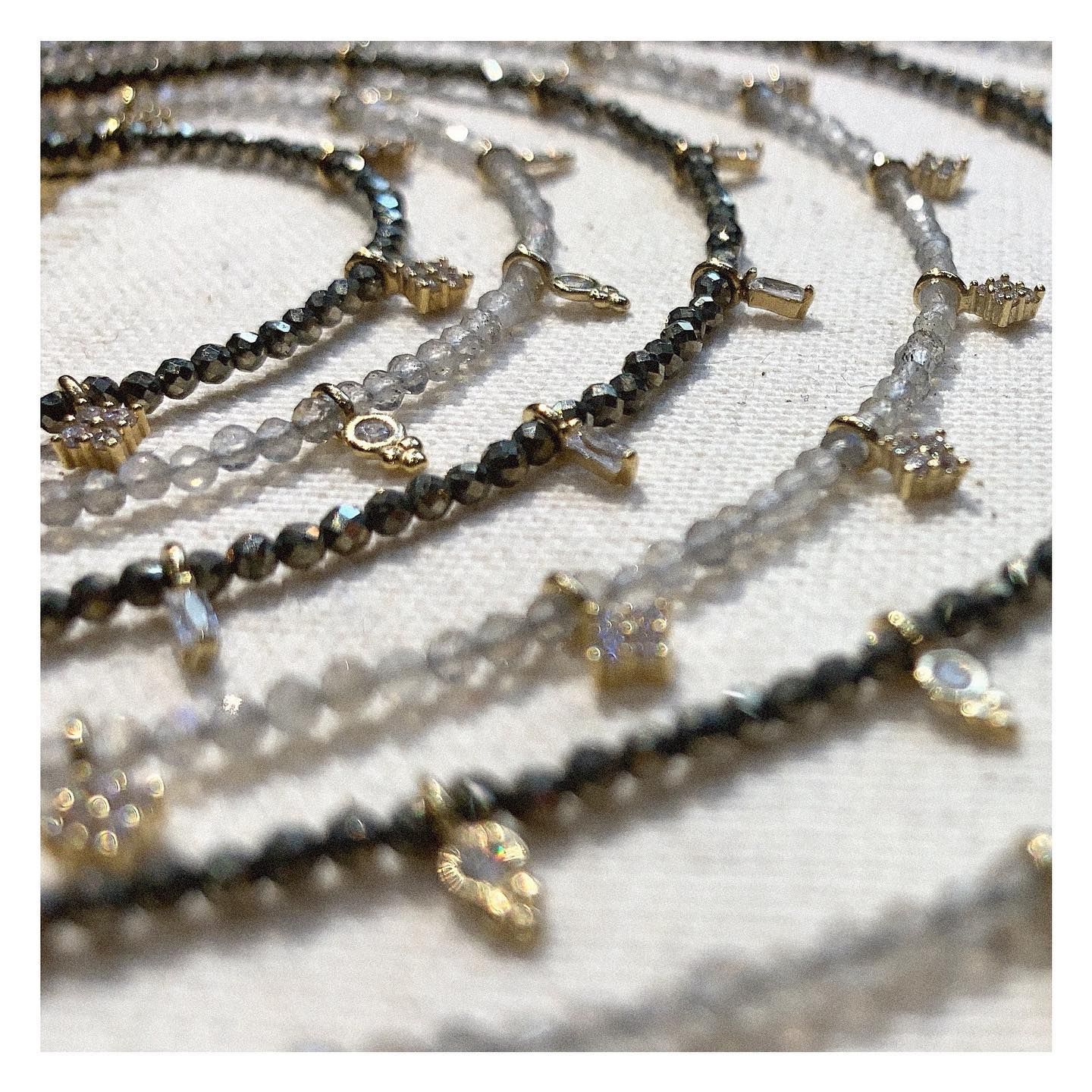 Gros plan de plusieurs colliers de perles avec des breloques en or sur une surface blanche.