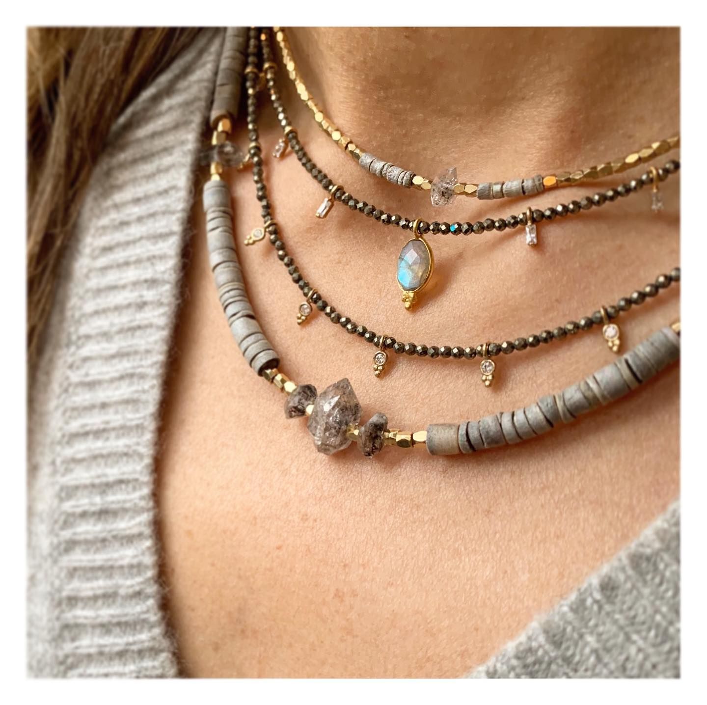 Gros plan d'une personne portant quatre colliers superposés : gris, or et perles.
