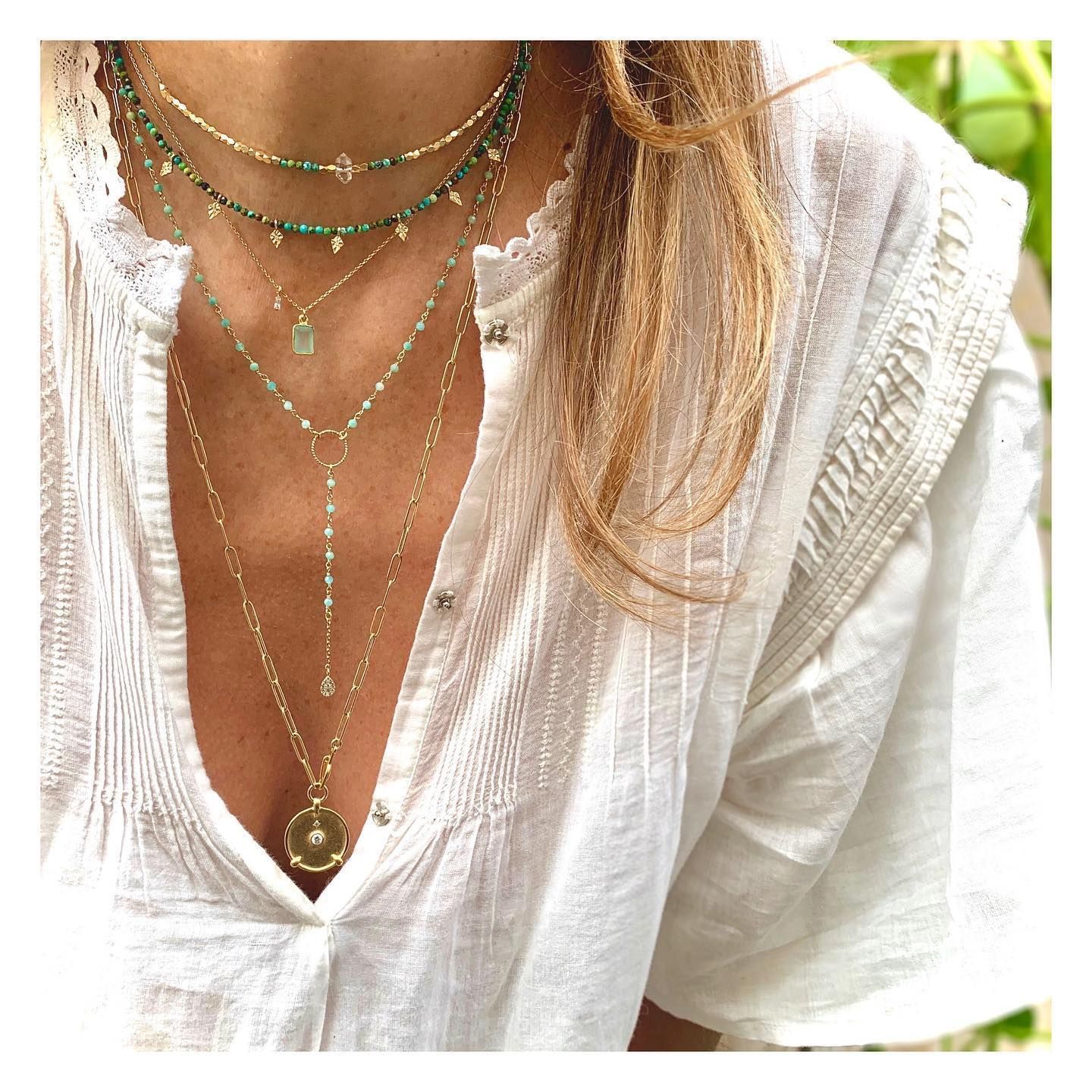 Femme portant plusieurs colliers en or, chemisier blanc ouvert.