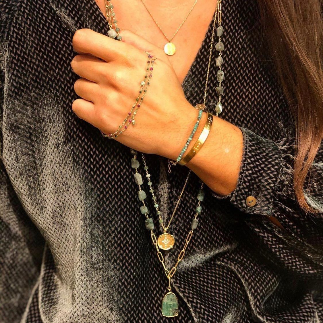 Personne portant des colliers et des bracelets en or superposés sur un haut texturé foncé.
