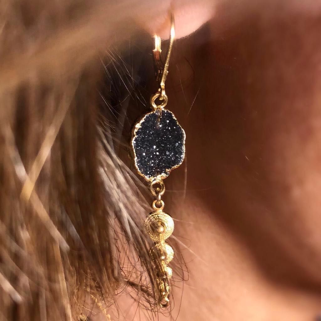 Boucle d'oreille en or avec pierre foncée texturée et perles d'or suspendues.