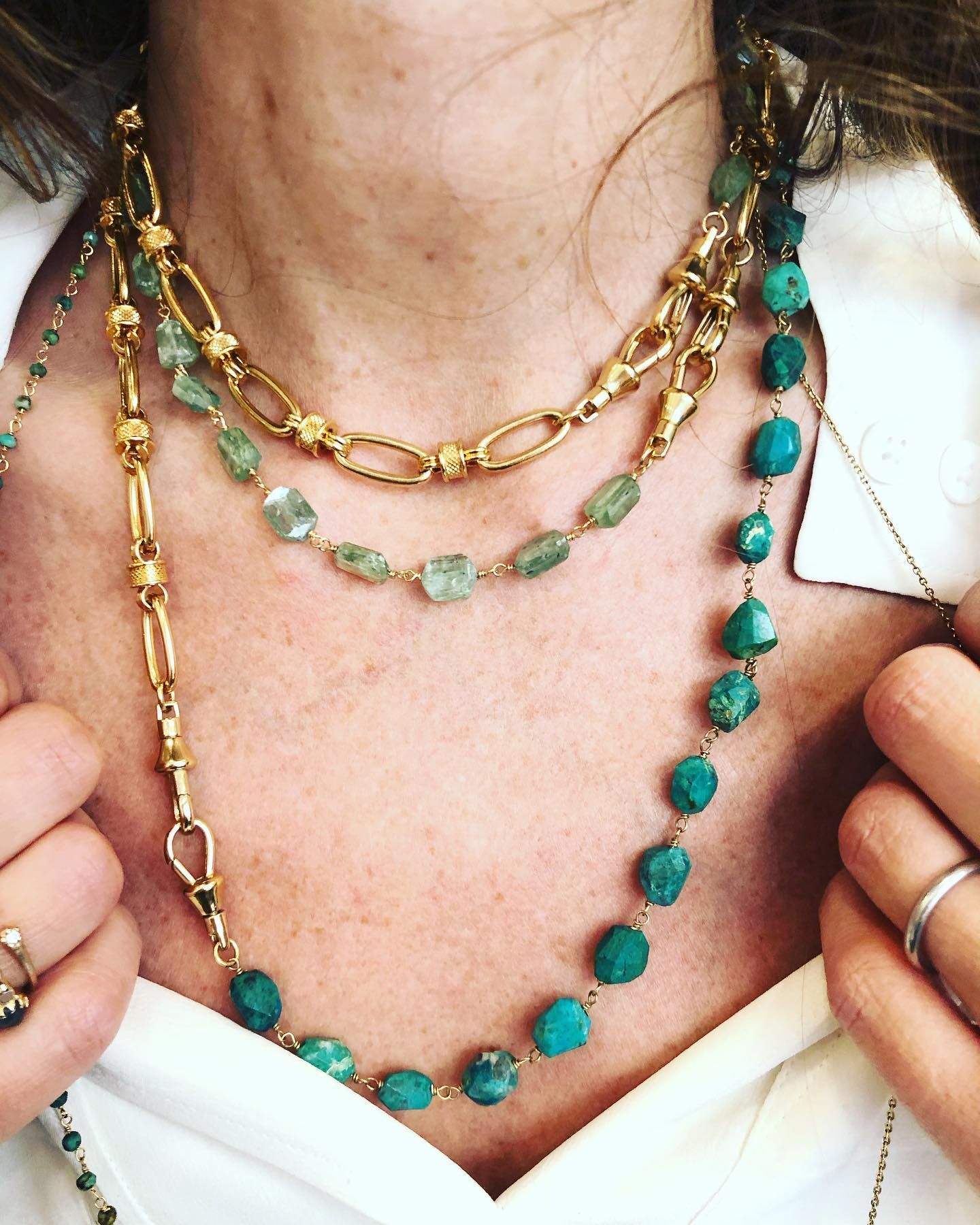 Femme portant des colliers en or superposés avec des pierres précieuses turquoises et vertes.