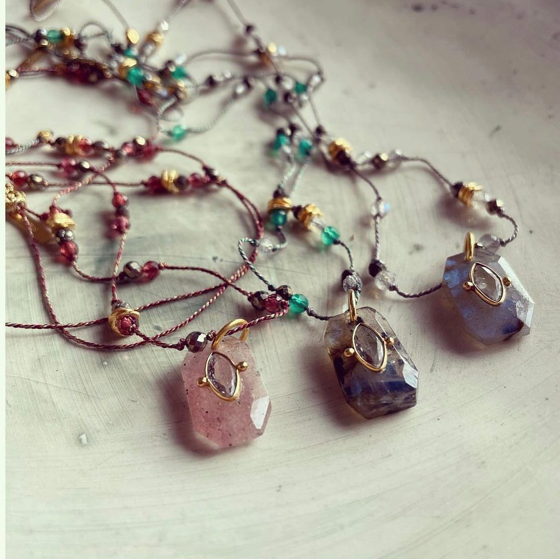Gros plan de trois colliers avec des pendentifs en pierres précieuses colorées et des chaînes de perles sur une surface blanche.