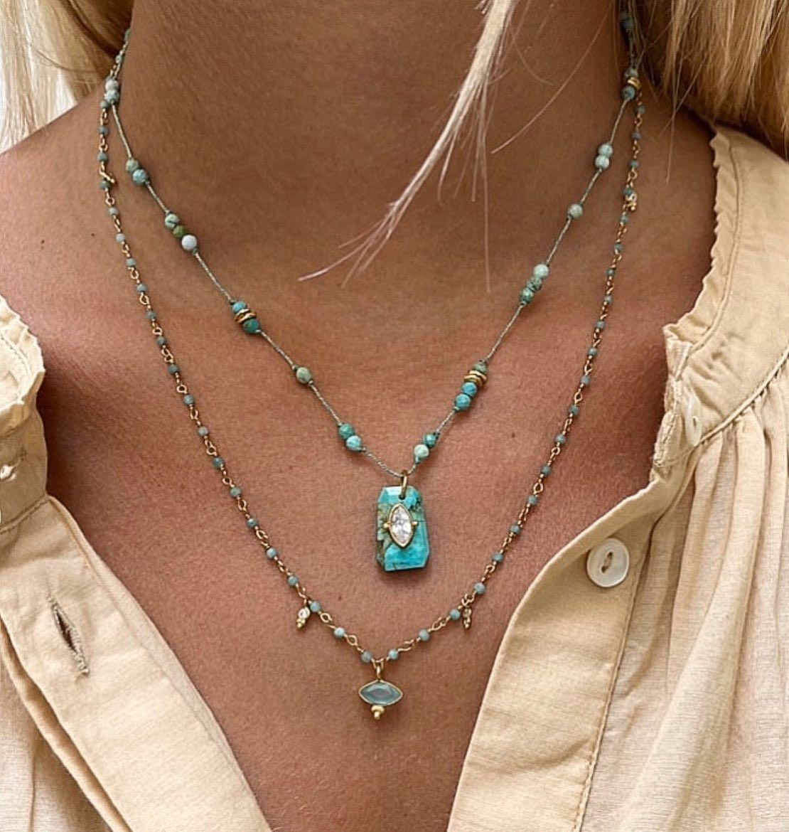 Deux colliers de perles turquoise sur une personne portant un chemisier beige.
