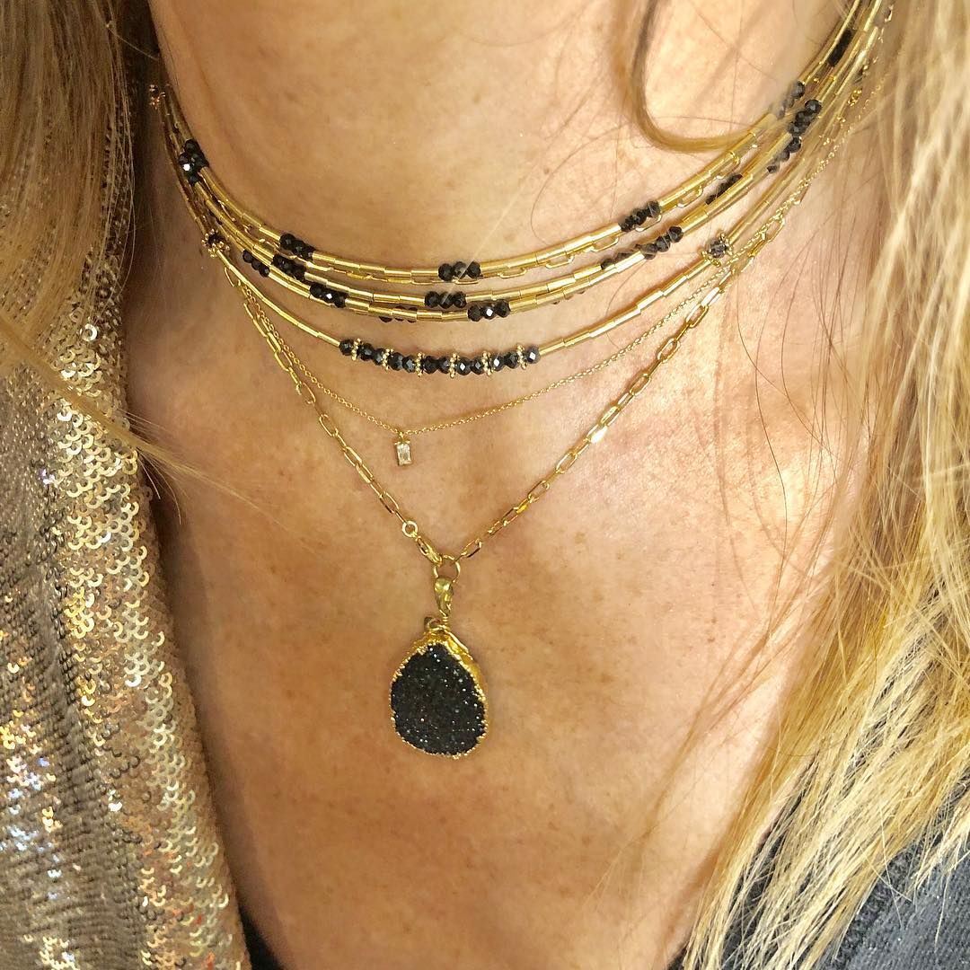Femme portant des colliers en or superposés avec des perles noires et un pendentif en forme de larme.