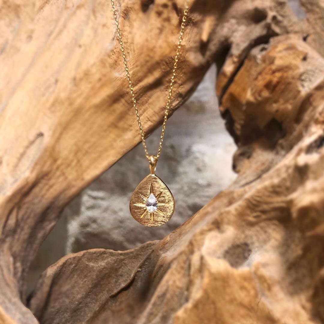 Collier pendentif en forme de larme en or sur fond bois.