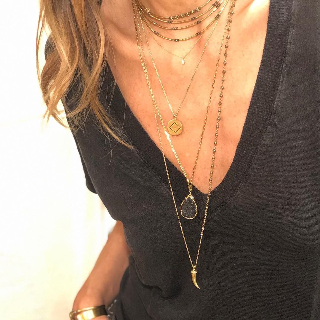 Femme portant un haut noir et plusieurs colliers en or superposés.