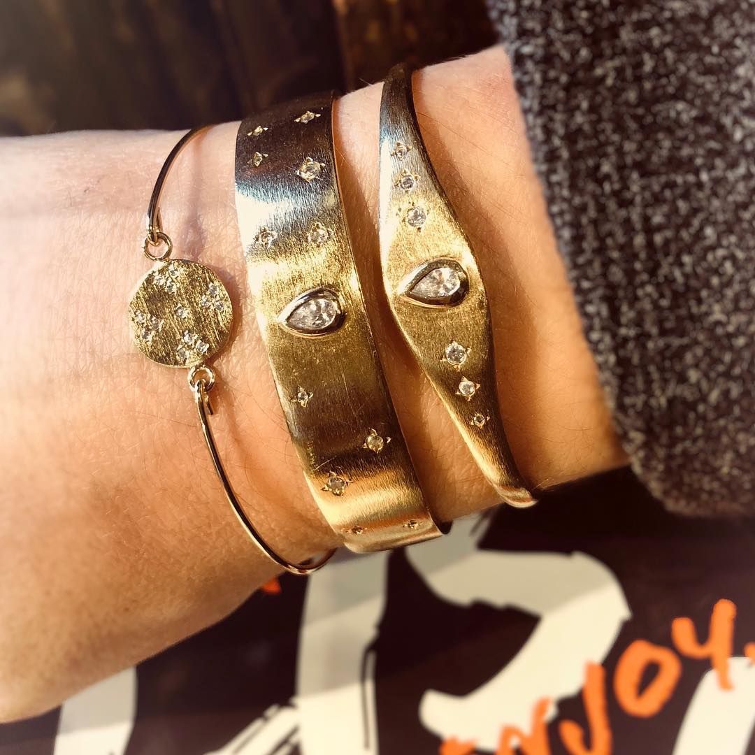 Gros plan d'un poignet orné de trois bracelets en or. L'un est une chaîne fine, les deux autres sont épais et sertis de diamants.