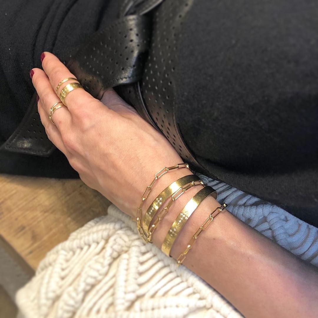 Bras de femme avec bracelets et bagues en or, posé sur un haut noir, avec une couverture tricotée blanche.