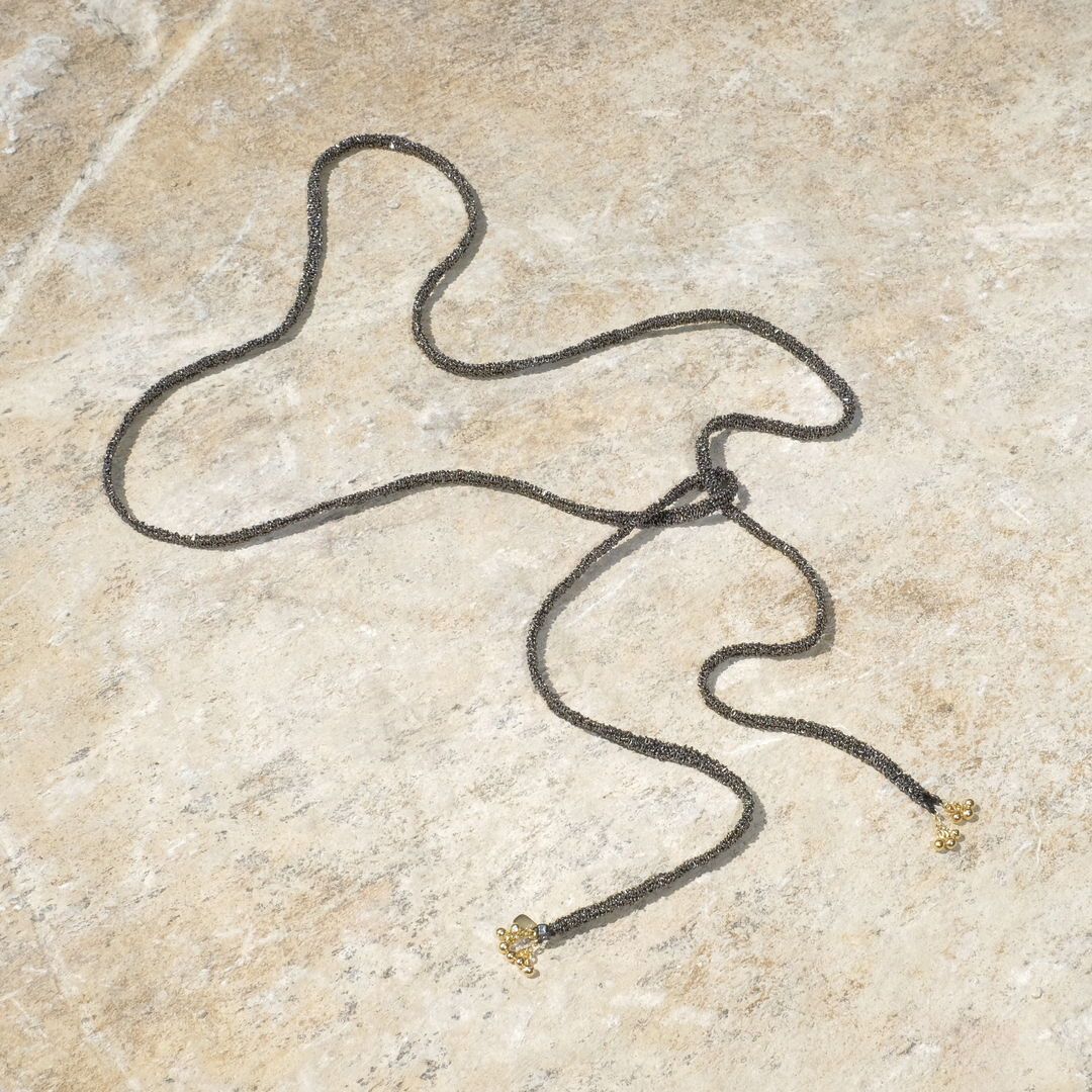 Collier de perles noires sur une surface en pierre beige. Le collier est noué avec des fermoirs dorés.