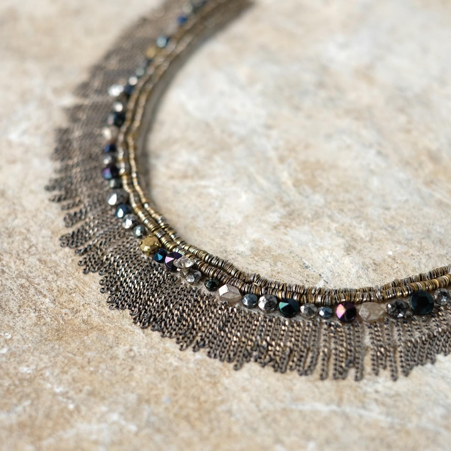 Gros plan d'un collier en or antique perlé avec des détails de franges sur une surface en pierre.