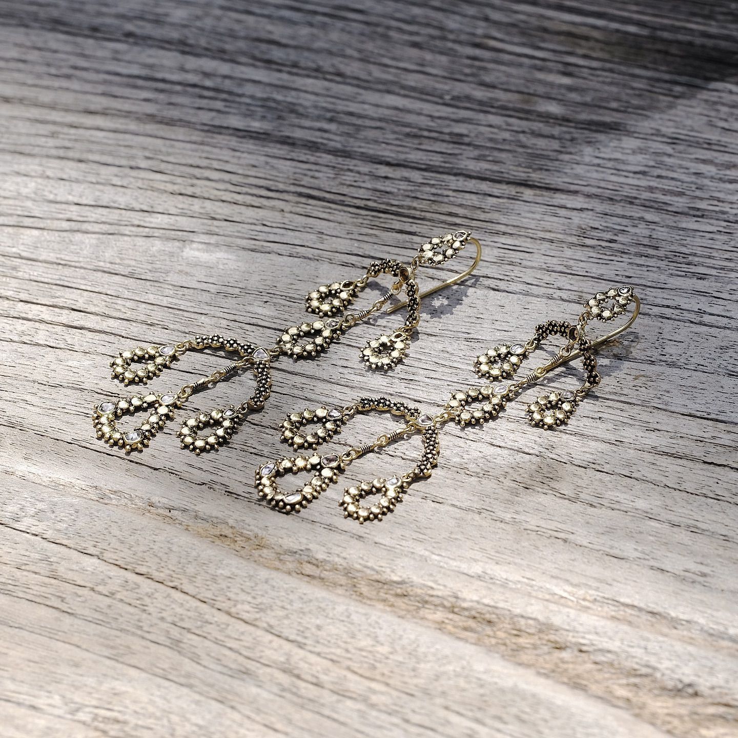 Boucles d'oreilles pendantes en or antique avec de petites pierres précieuses sur une surface en bois patiné.