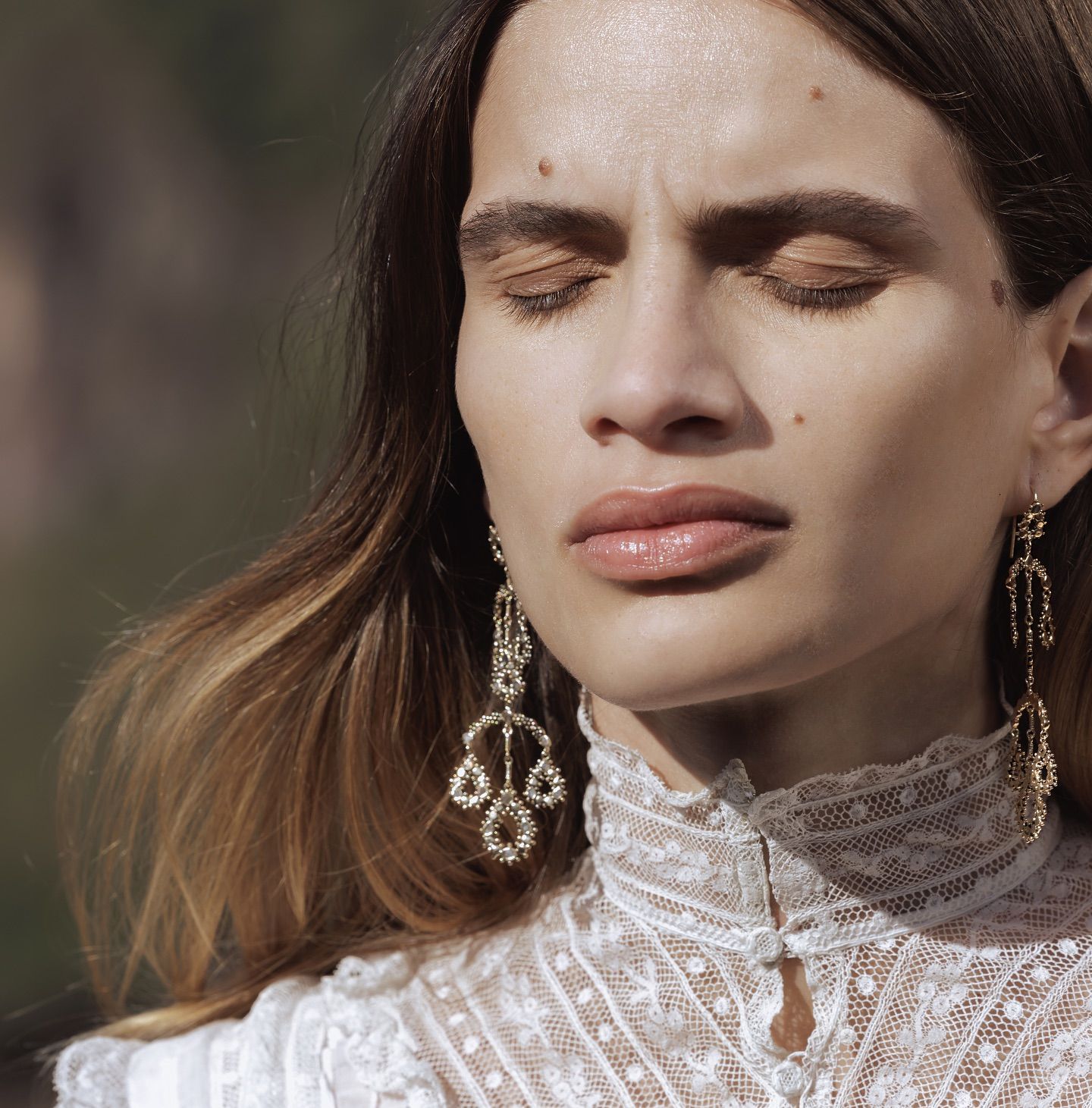 Femme aux yeux fermés, portant de la dentelle et des boucles d'oreilles ornées, à l'extérieur, au soleil.