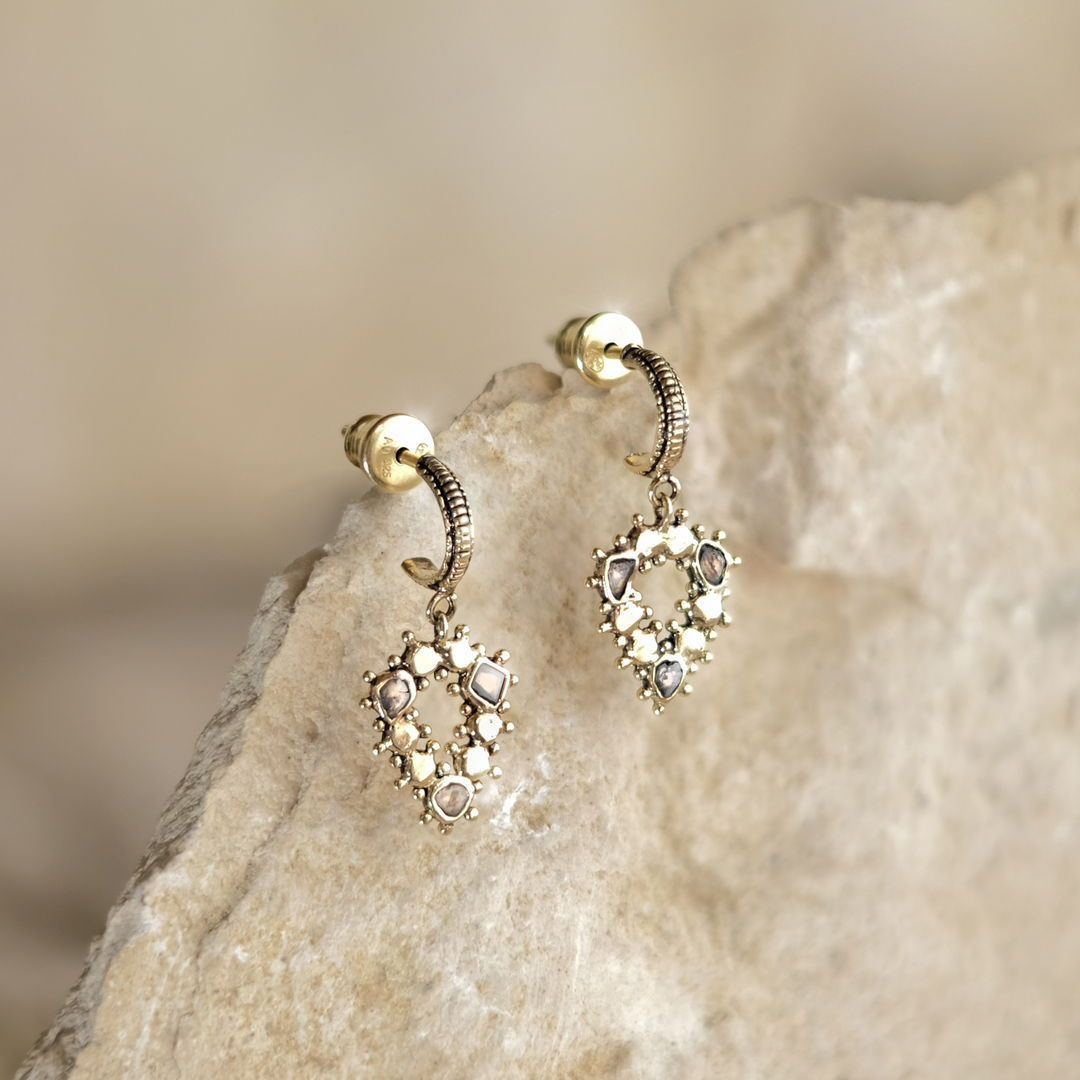 Boucles d'oreilles en or avec des accents de pierres précieuses, reposant sur une surface rocheuse beige.