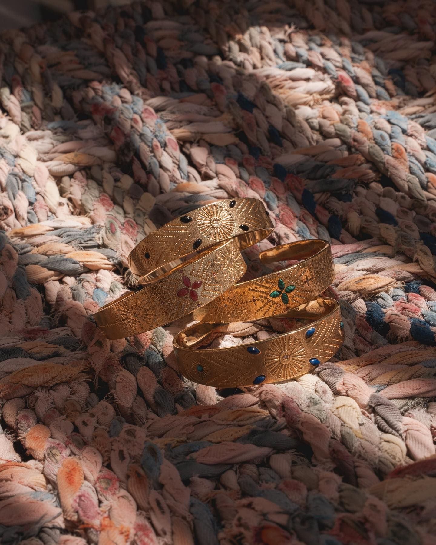 Bracelets en or avec pierres précieuses sur une couverture texturée.