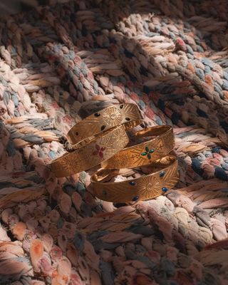 Bracelets en or avec pierres précieuses sur une surface tissée avec un éclairage chaleureux.
