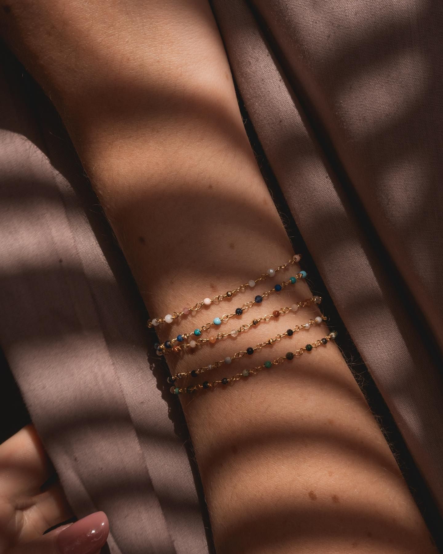 Bras avec plusieurs bracelets en chaîne dorée, ornés de perles colorées.