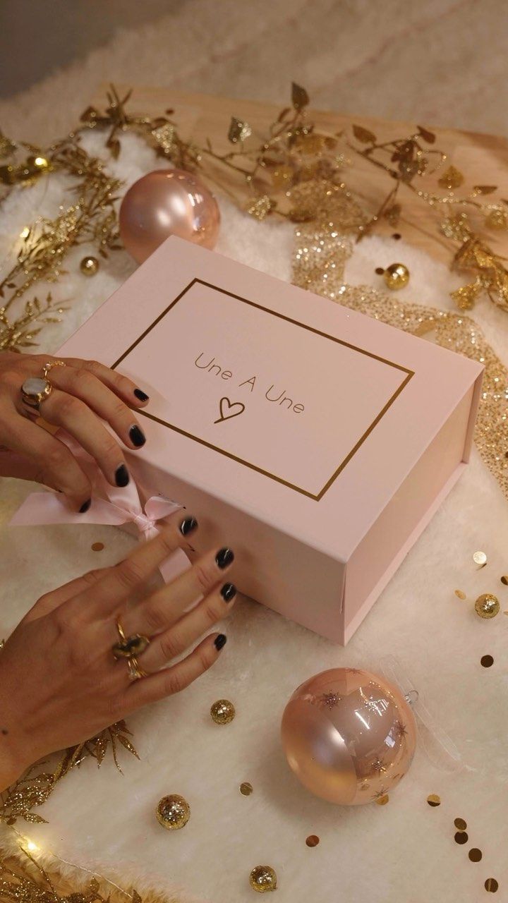 Les mains ouvrent une boîte cadeau rose avec des accents et des décorations dorés.