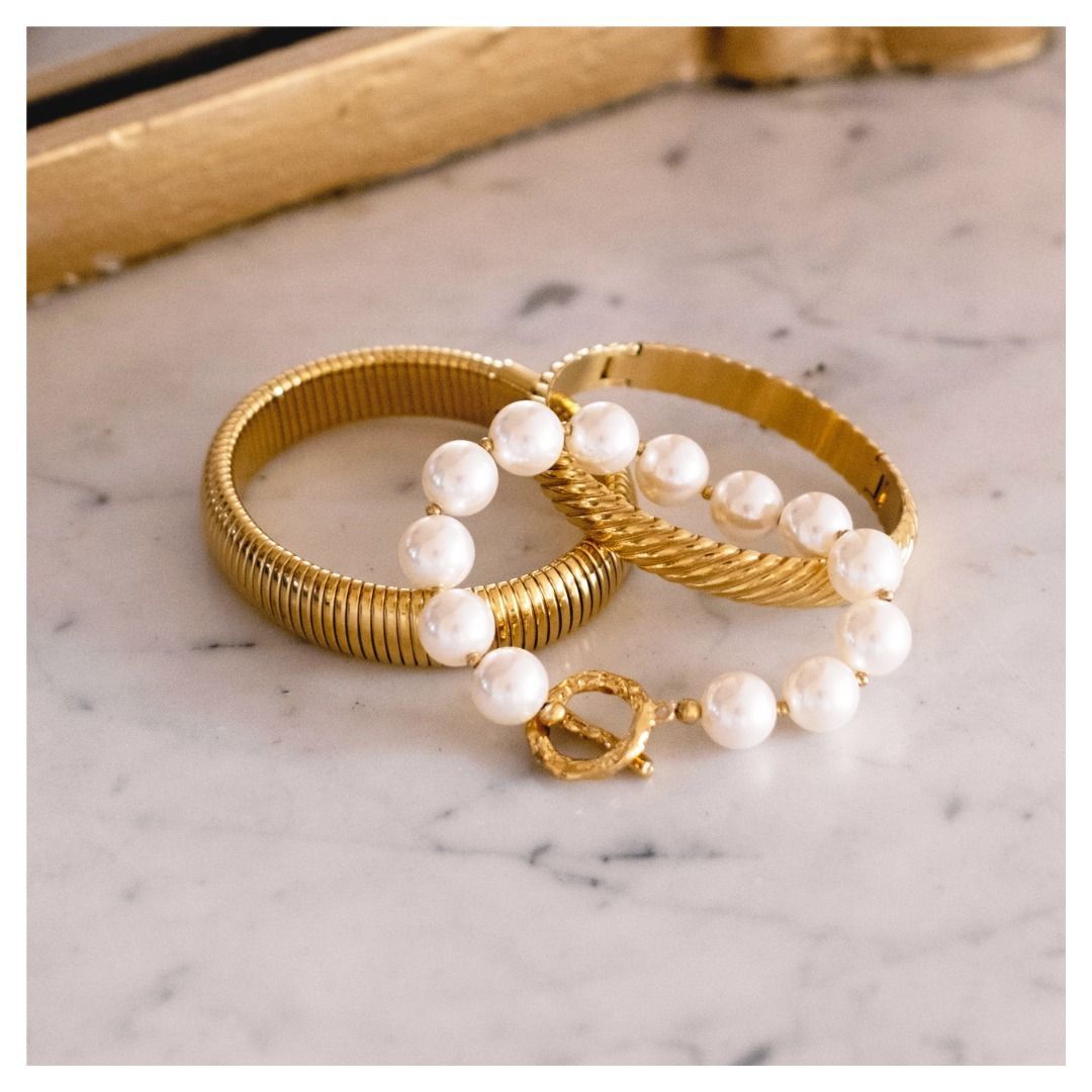 Bracelets en or et bracelet en perles sur une surface en marbre blanc.