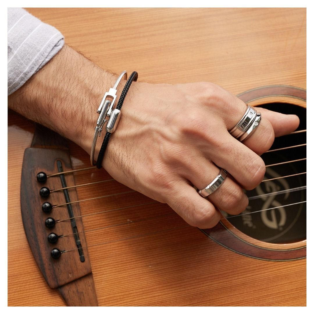 Main d'homme jouant de la guitare, portant bagues et bracelets. L'accent est mis sur la main et les instruments.