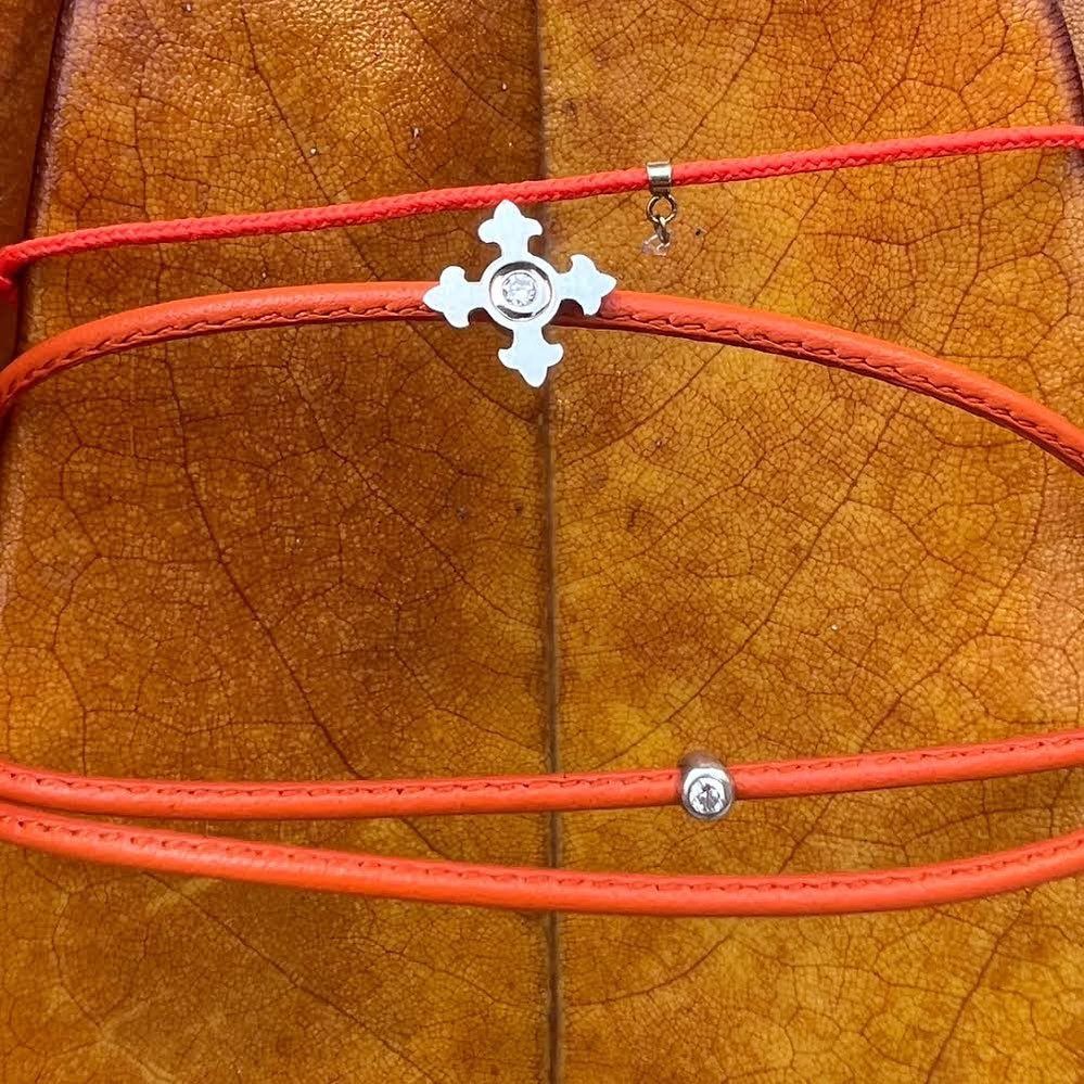 Colliers en cuir rouge avec breloques en argent, posés sur une feuille marron texturée.