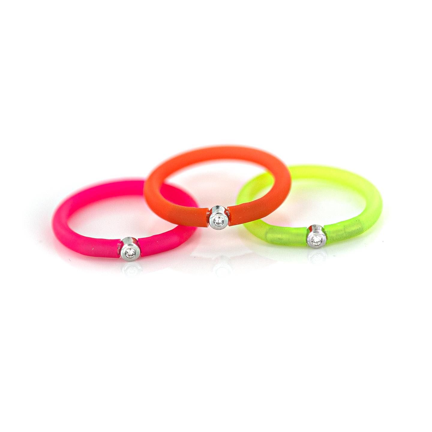Trois anneaux colorés : rose, orange et vert fluo, chacun avec une petite breloque argentée.