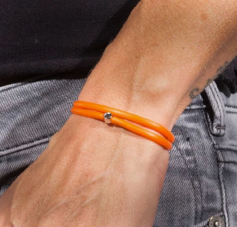Gros plan du poignet d'une personne portant un bracelet orange. Ce bracelet est composé de deux cordons orange maintenus ensemble par un petit fermoir en argent.