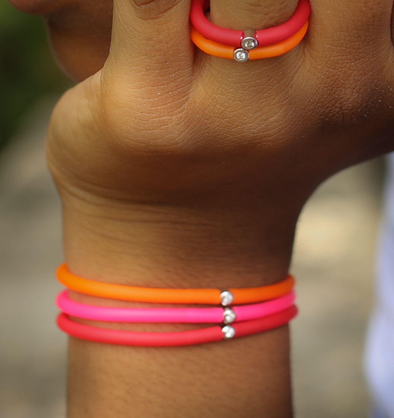 Main portant des bracelets et une bague orange et rose, chacun avec un petit accent de diamant.