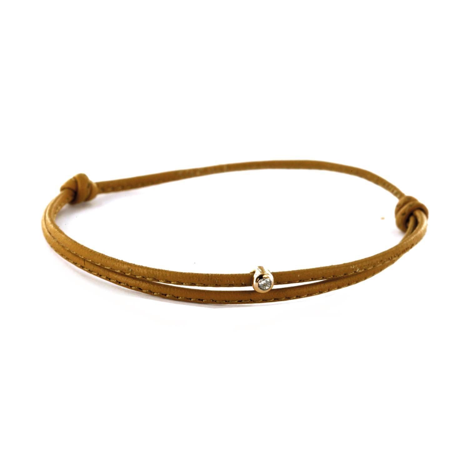 Bracelet en or avec un seul pendentif en diamant et cordon marron.