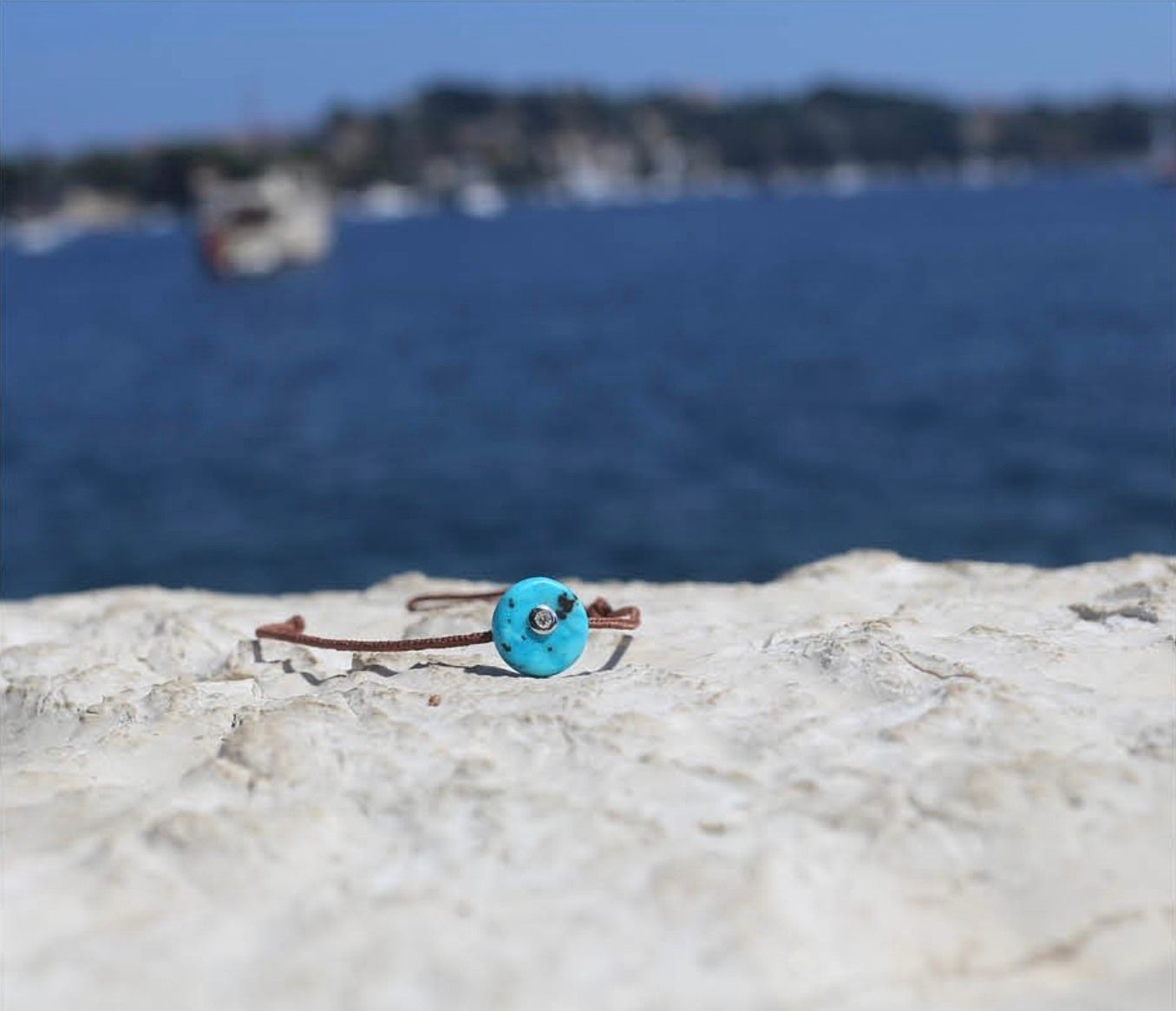 Bracelet avec perle turquoise sur rocher, surplombant l'eau bleue.