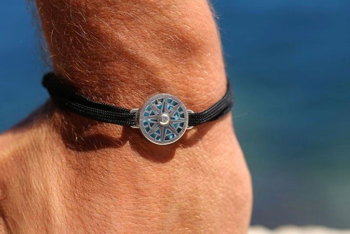 Gros plan d'un poignet avec un bracelet en cordon noir orné d'une breloque en forme de rose des vents.