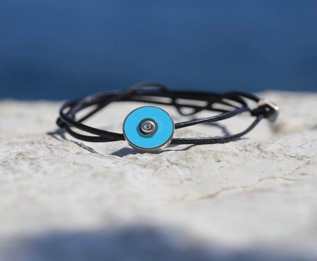 Bracelet en fil noir avec breloque circulaire turquoise, sur fond bleu flou.
