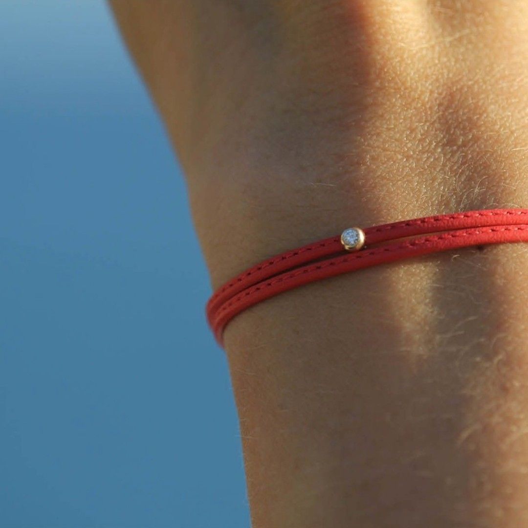Poignet avec un bracelet rouge et une petite perle argentée sur fond bleu.